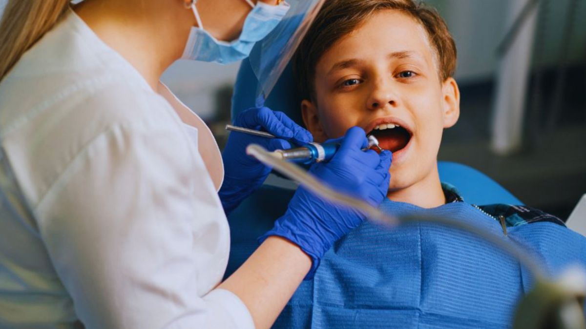 A pediatric dentist examines a young boy's teeth during a routine dental check-up in a dental clinic.