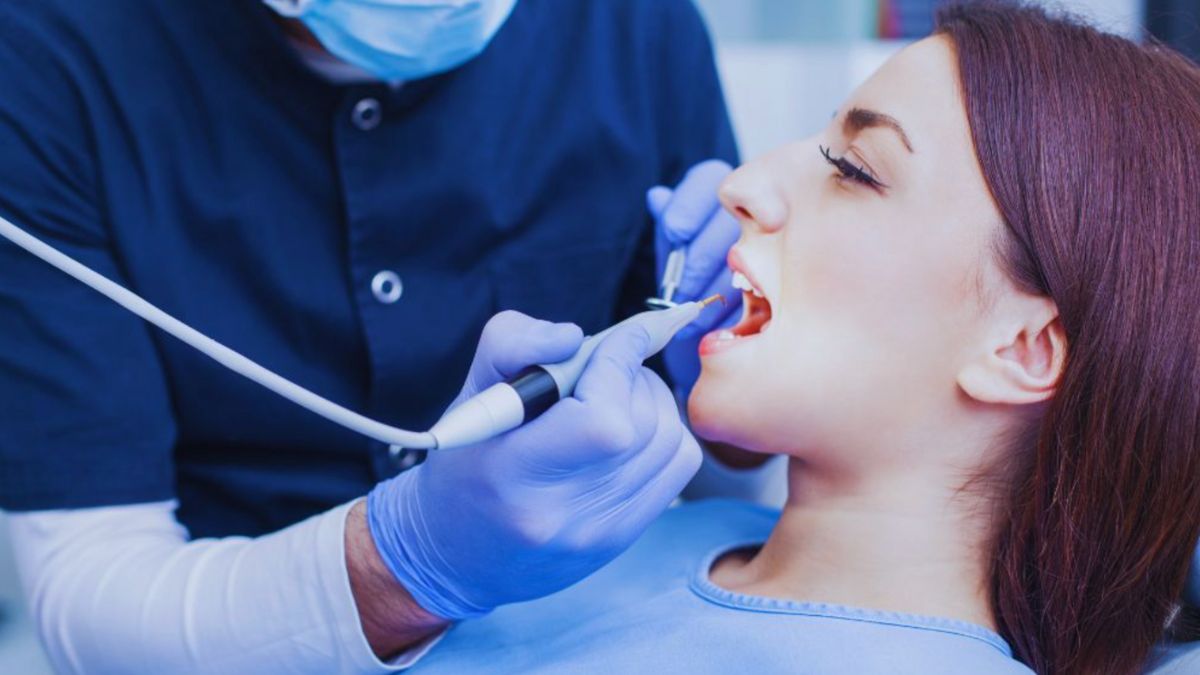 A woman receiving a dental cleaning from a dentist in a clinical setting showcasing oral hygiene practices.