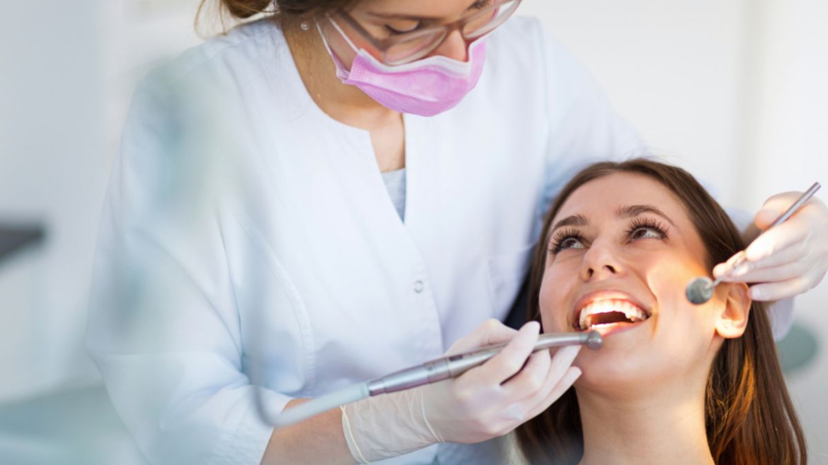 A dentist checks a woman's teeth during a dental examination in a clinical setting.