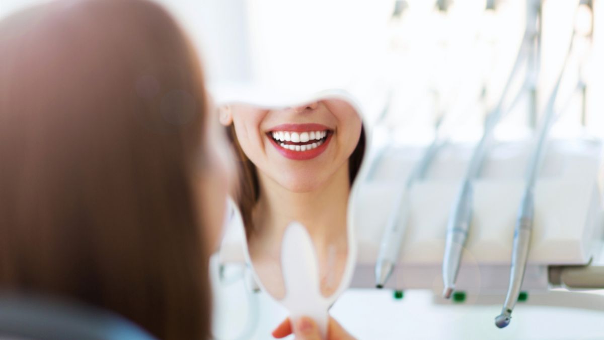 A woman examines her teeth in the mirror, likely after a dental appointment.