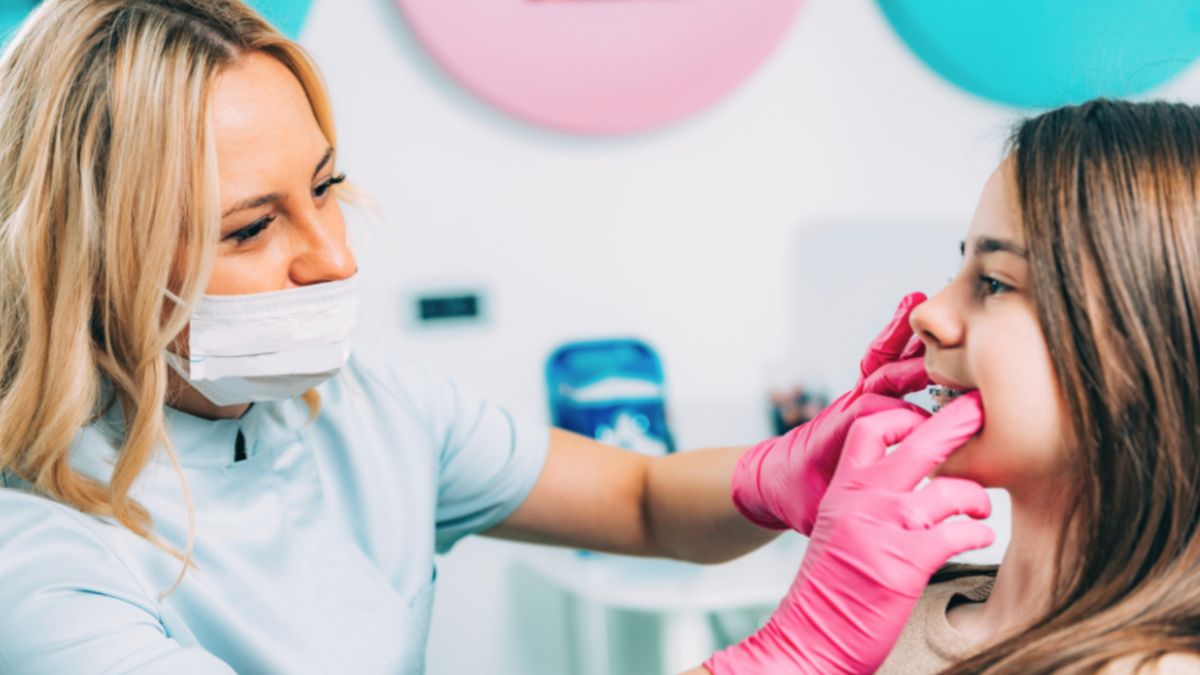 A girl with braces is having her teeth examined by a dentist in a clinical setting.