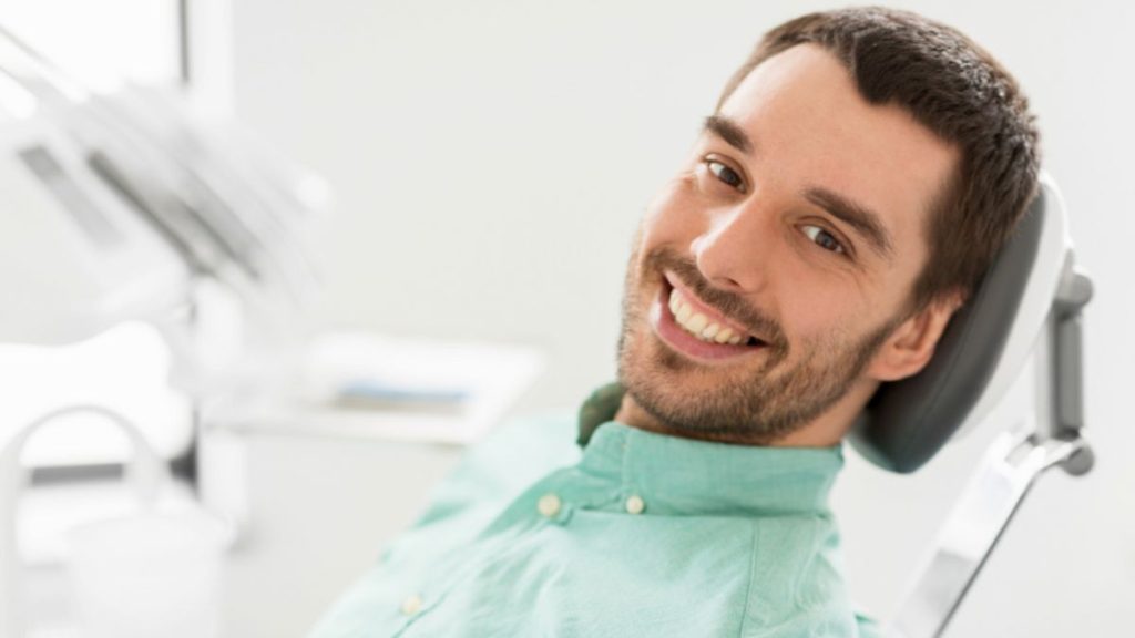 A man smiling broadly while sitting on a dental chair.