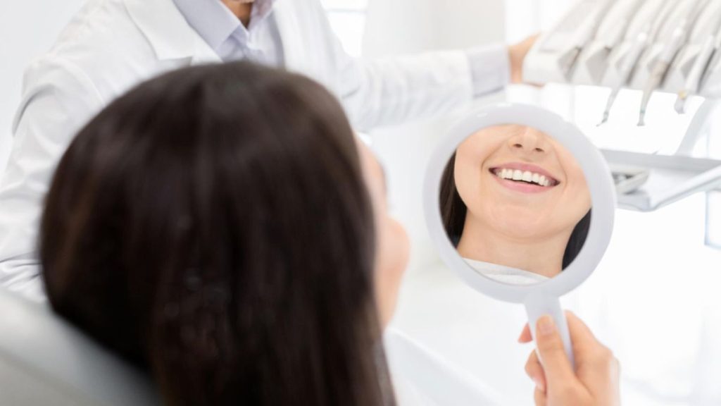 A woman examines her teeth in a mirror, reflecting the quality care at Smiles Dentistry in Lantana, FL.