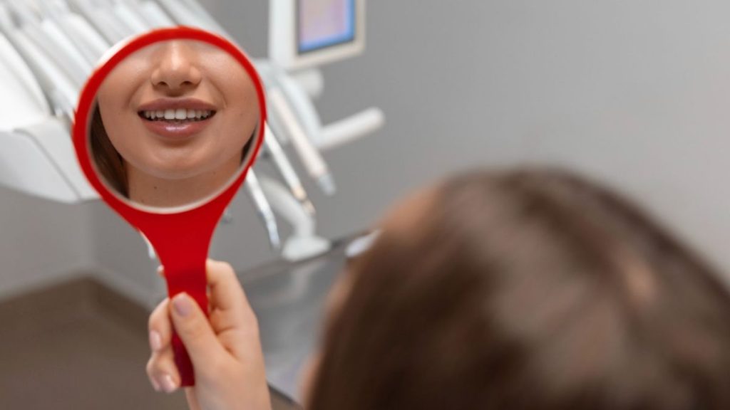 A woman checking her teeth in a mirror, emphasizing the importance of dental care in Wellington, FL.