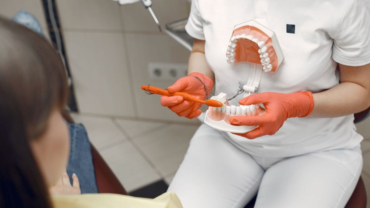 A woman in a dental chair with a toothbrush demonstrating dental care to a patient.