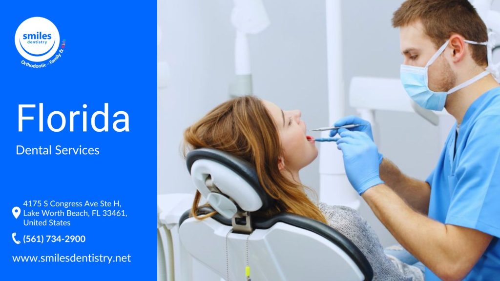 Dental Services Family Dentist A dentist wearing blue scrubs, gloves, and a face mask is examining a female patient in a modern dental clinic. The patient is in a dental chair with her mouth open while the dentist uses a dental mirror and tool for the examination.
