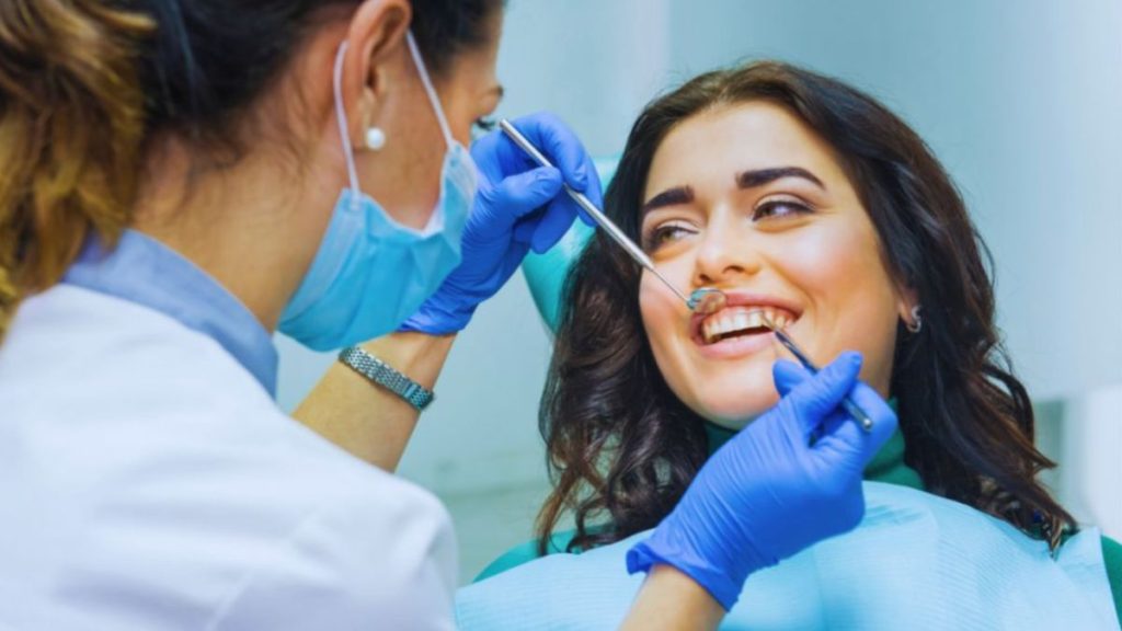A cosmetic dentist examines a smiling female patient's teeth during a consultation.
