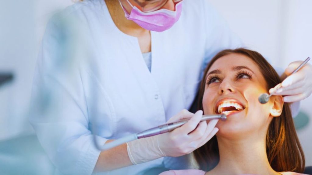 Female cosmetic dentist examines patient's smile with dental tools in a modern clinic.