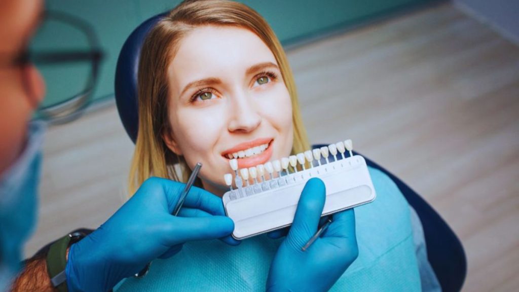 Dentist matching tooth shade for a smiling woman during a dental veneer consultation in Lake Worth Beach.