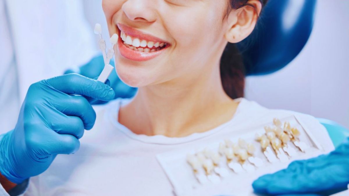 A smiling woman at a dental clinic has her teeth shade matched for dental veneers by a dentist wearing blue gloves in Lake Worth Beach.