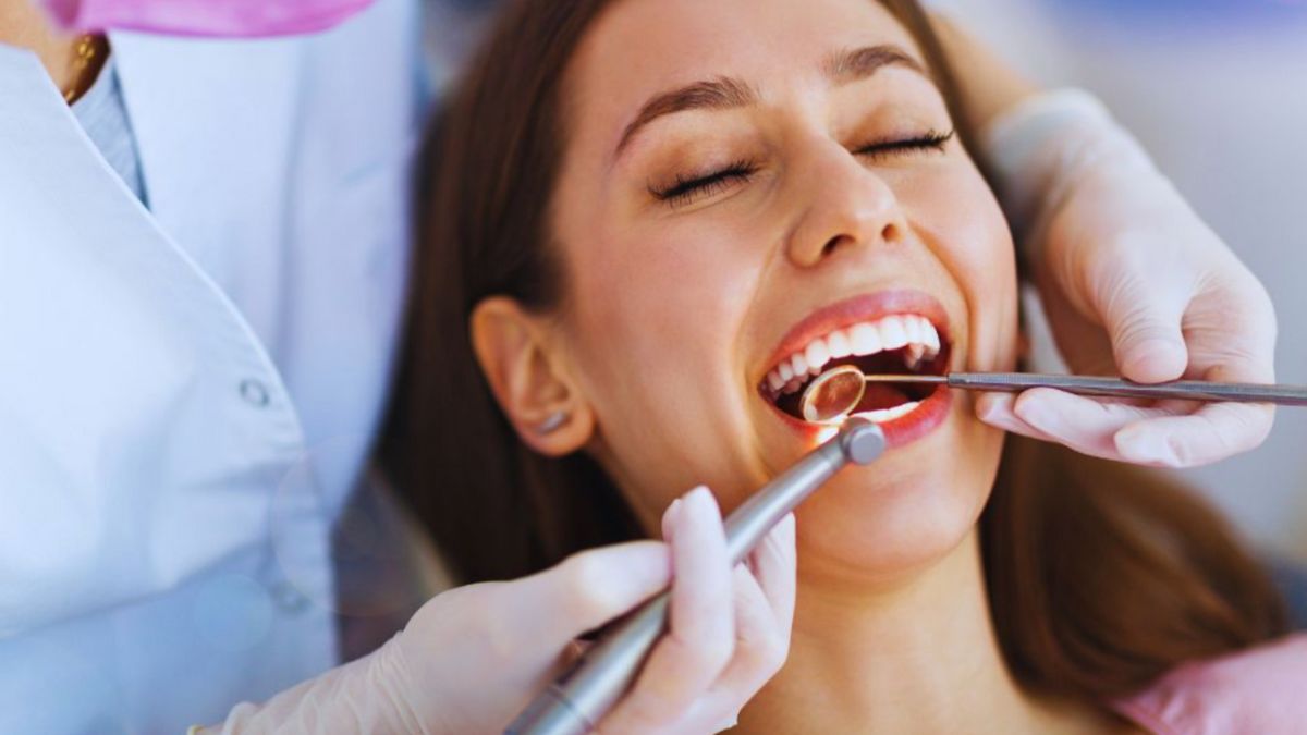 A woman smiles while a dentist in Lake Worth, FL, performs a checkup using a dental mirror and scaler.