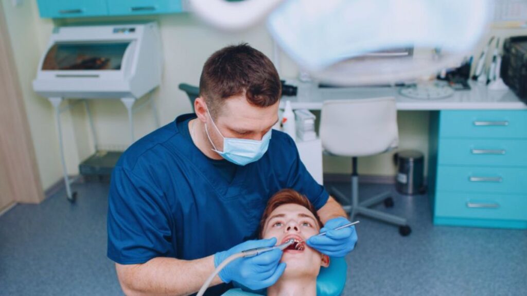 A male dentist in blue scrubs examines a young patient’s teeth in a modern dental clinic in Lake Worth, FL.