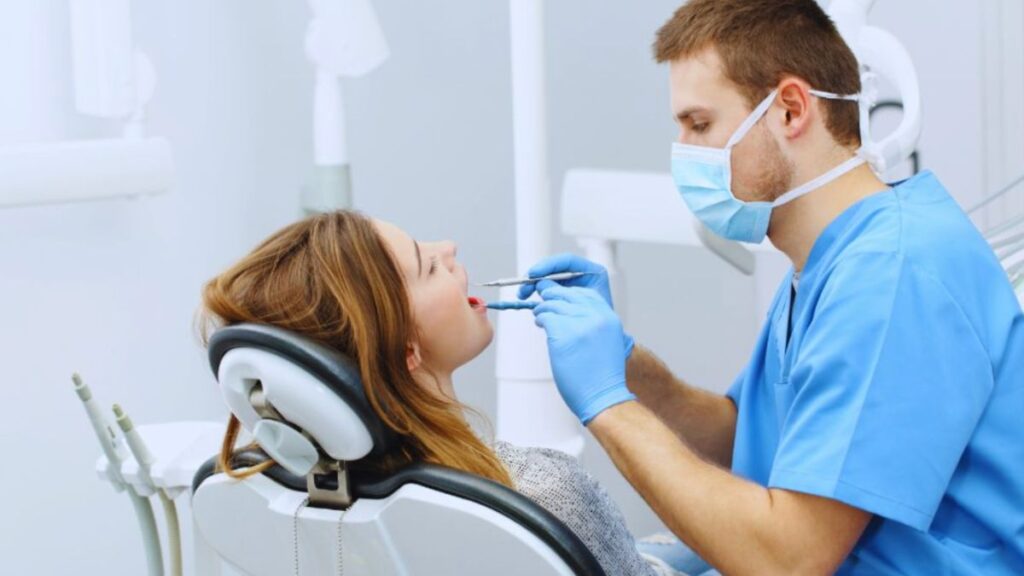 A dentist examines a patient’s teeth in a well-lit, modern dental clinic; instruments and equipment are visible near the chair.