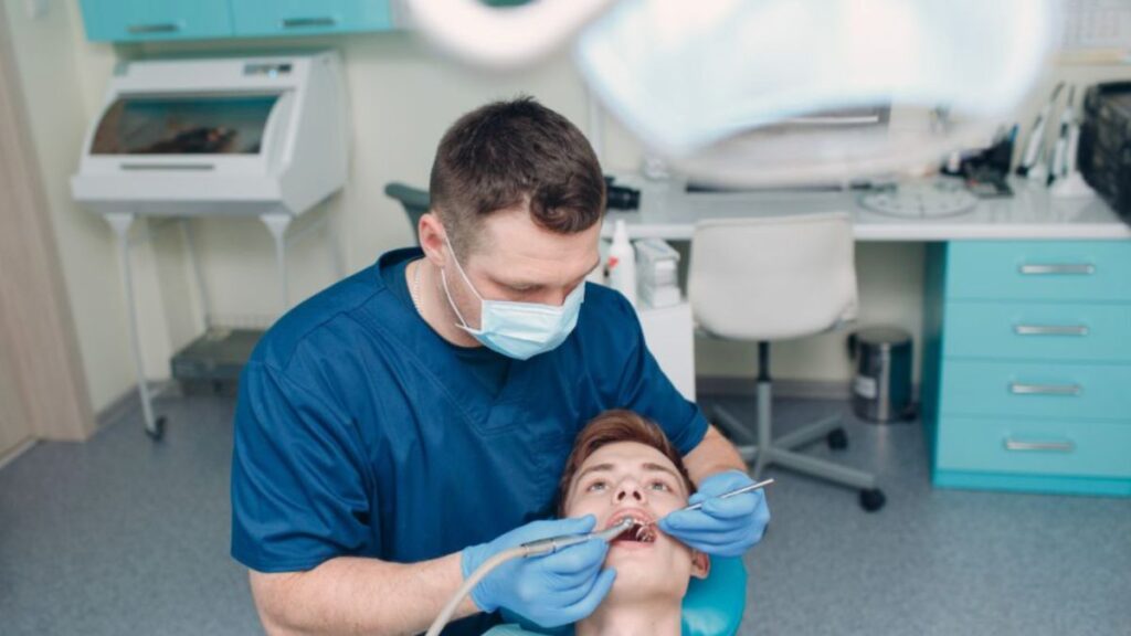 A dental professional in blue scrubs and gloves treats a patient in a modern Lake Worth Beach, FL clinic with clean cabinetry, dental tools, and contemporary equipment.