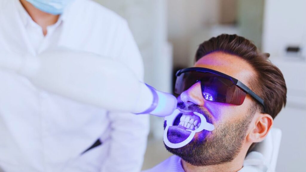 A man in a dental chair under a blue light for teeth whitening in Lake Worth.