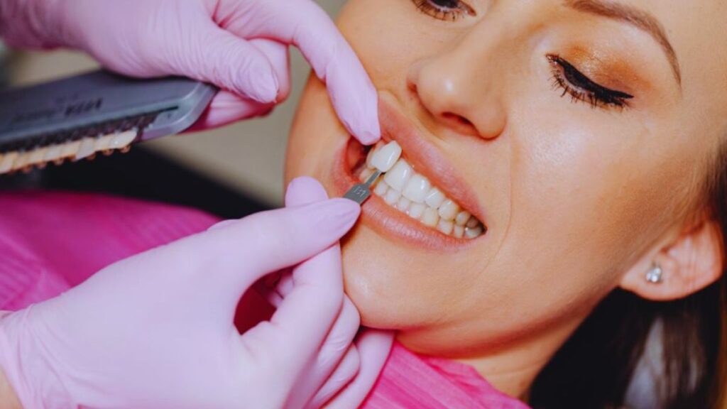 Dentist in pink gloves matches veneer shade to patient's teeth during consultation — Veneers in Lake Worth, FL.