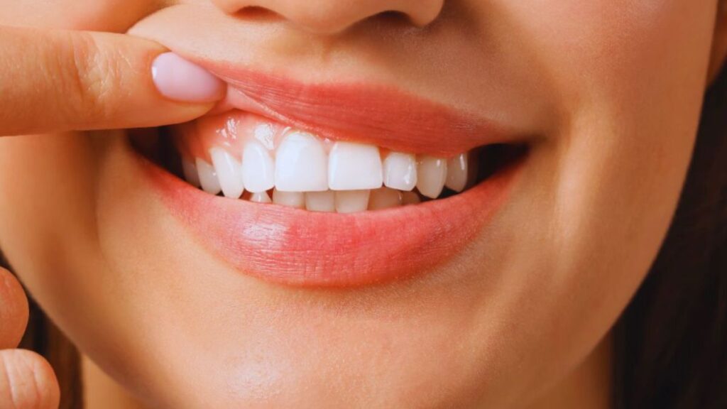 A woman gently touching her teeth, showcasing her healthy gums and a confident smile.