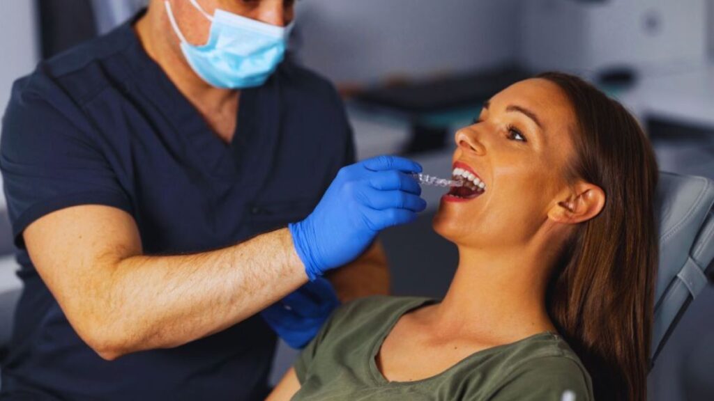 A family orthodontist in Boynton wearing blue gloves is assisting a patient in a treatment chair, likely providing orthodontic care in a modern clinic setting.