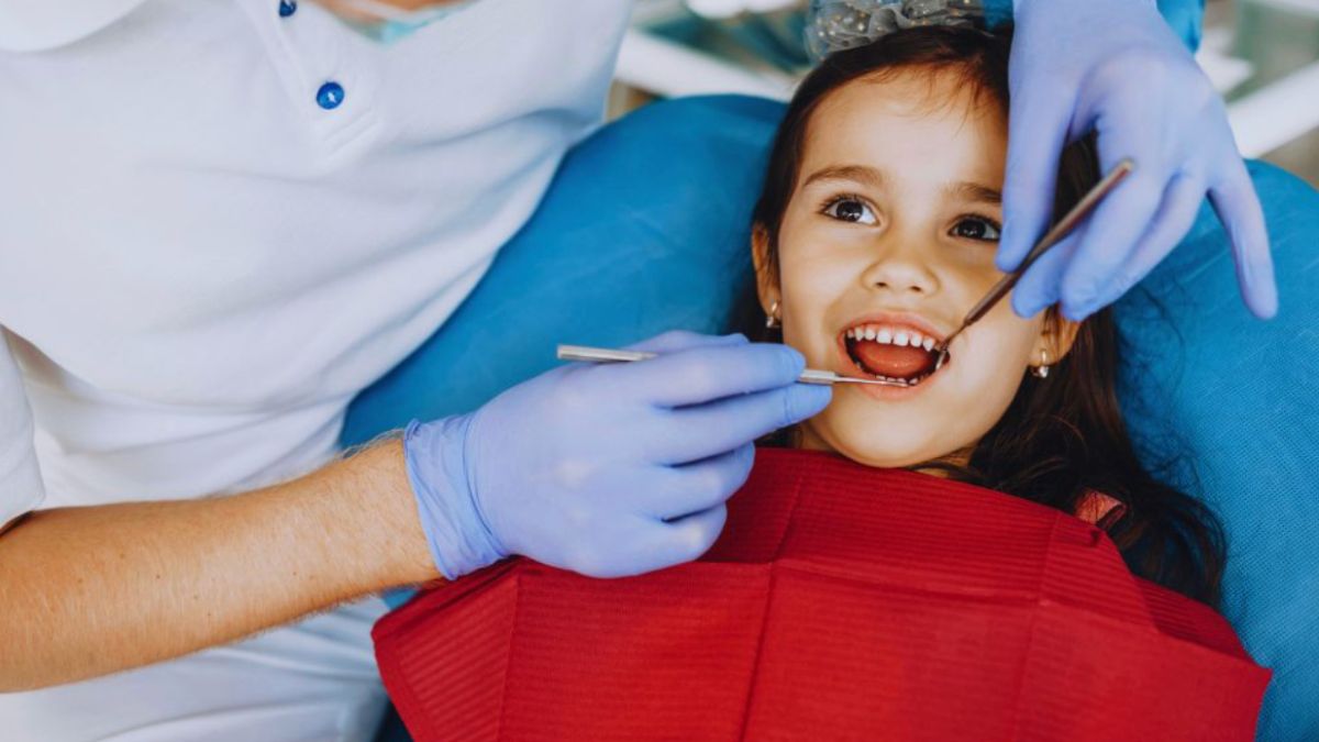 A pediatric dentist is checking the teeth of a smiling little girl in a welcoming dental office setting.