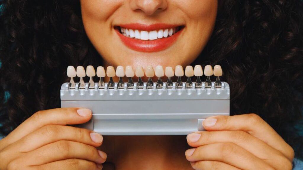 Woman smiling and holding a dental veneer shade guide to compare tooth color options for cosmetic dentistry.